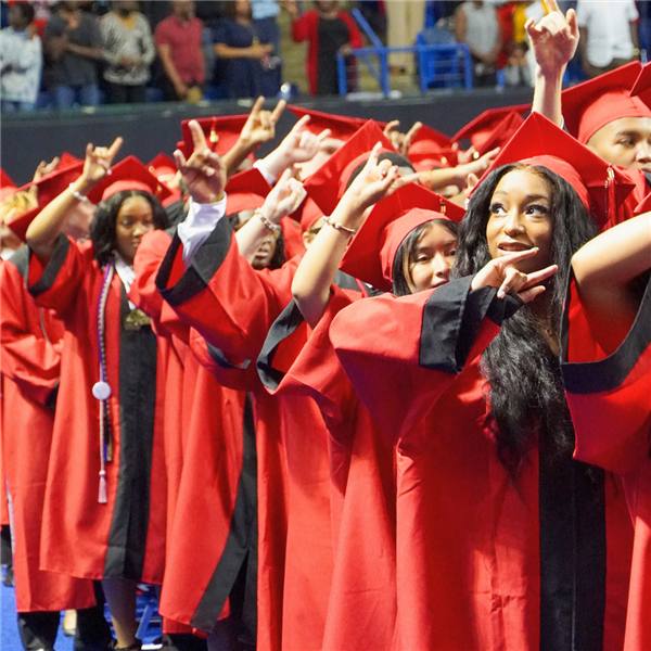  Graduates in red robes sing the Central High School alma mater with the horns up hand gesture.